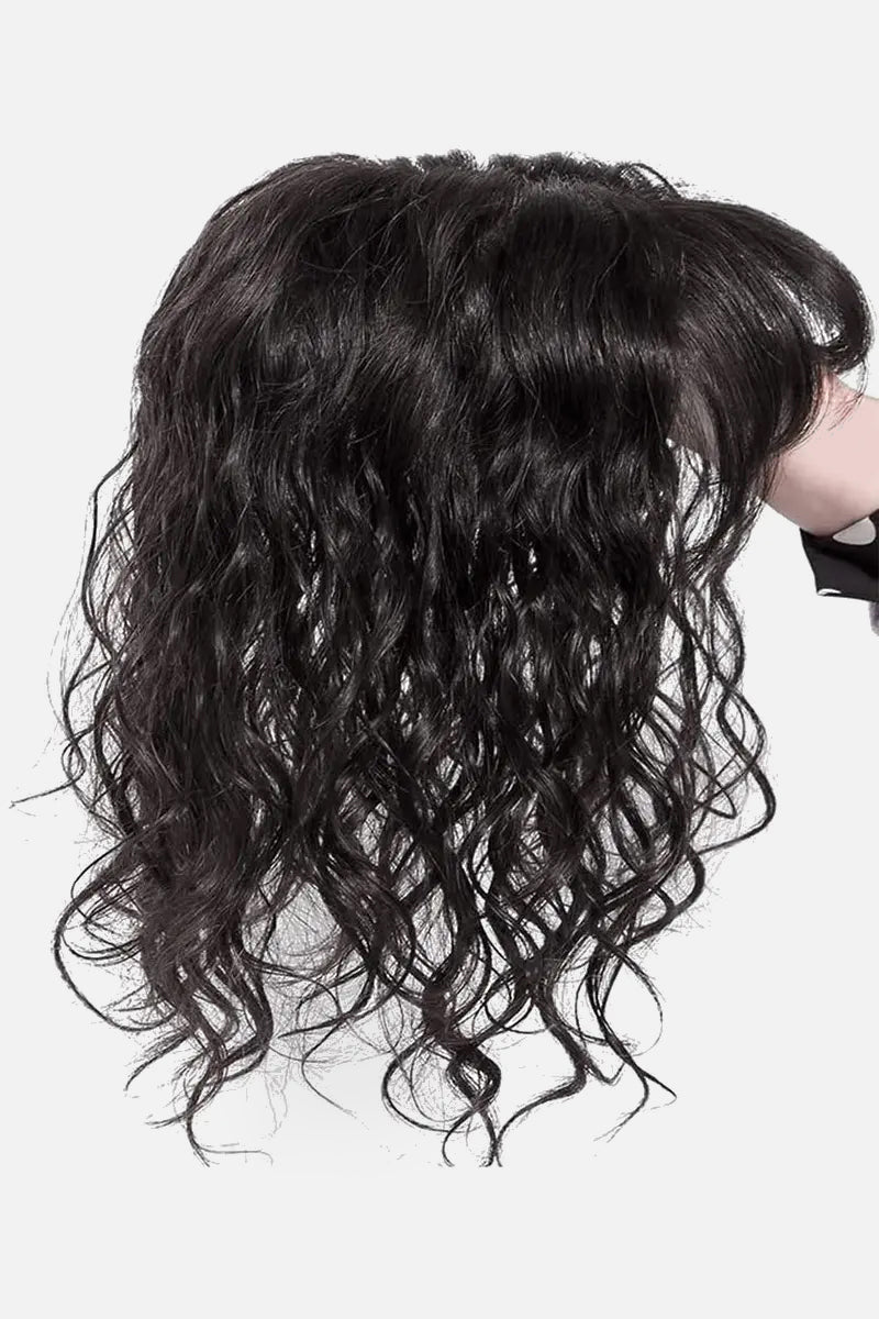 A curly human hair topper with bangs, showing the texture and volume of the hair.