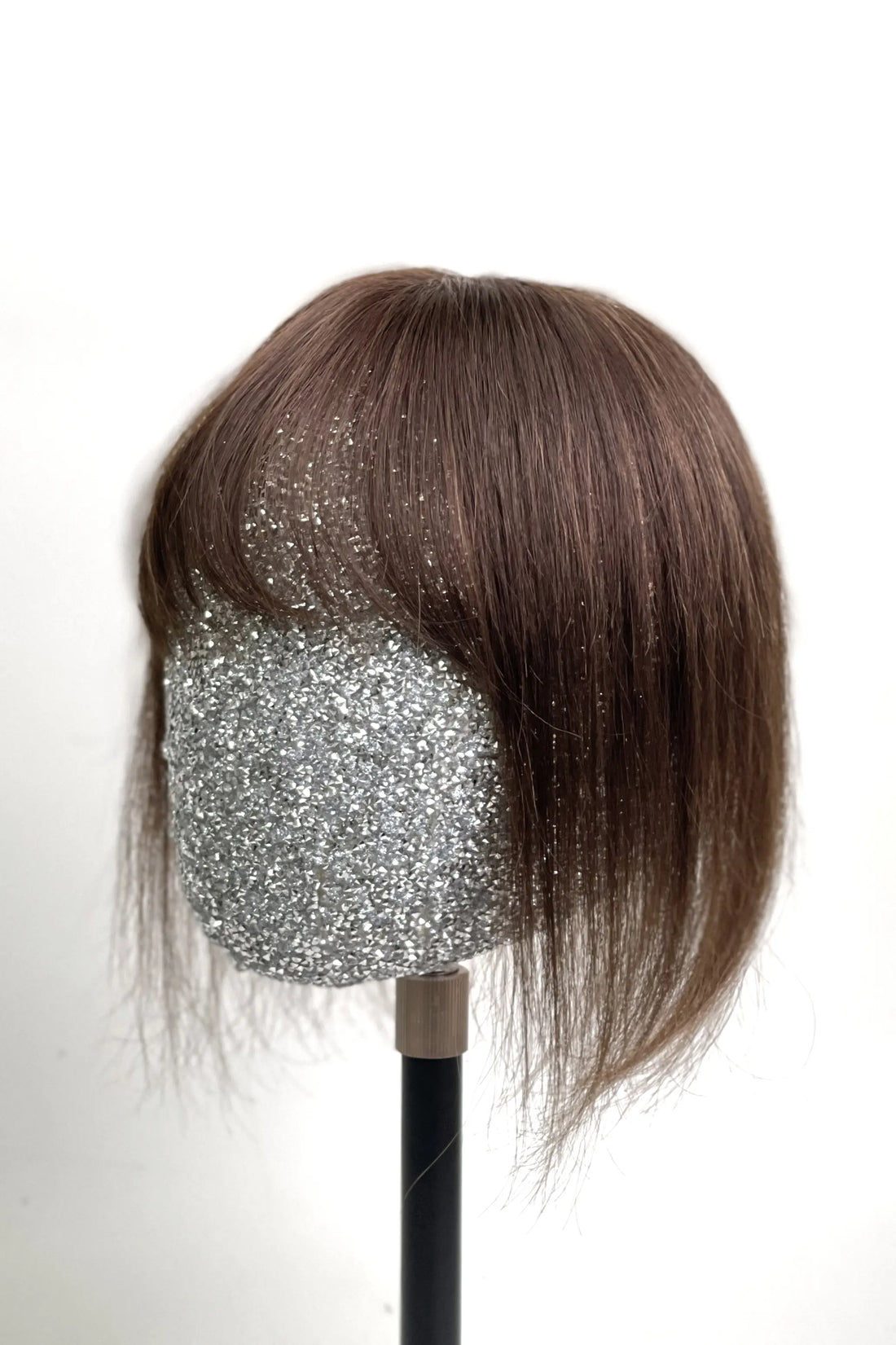 A mannequin head showcasing a medium brown human hair topper with bangs.