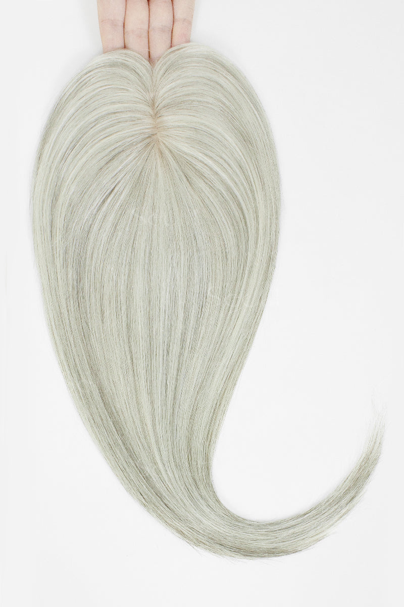 A pale icy ash blonde heart-shaped hair extension held up by a hand against a plain white background.