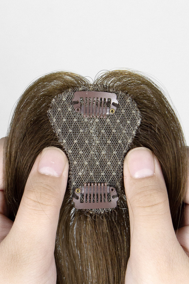 Hair topper with a mesh backing held between fingers against a neutral background