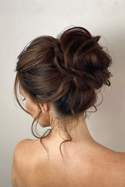 A woman shown from the back wearing a messy bun updo hairstyle with loose curls, in warm medium brown tones against a plain light background.