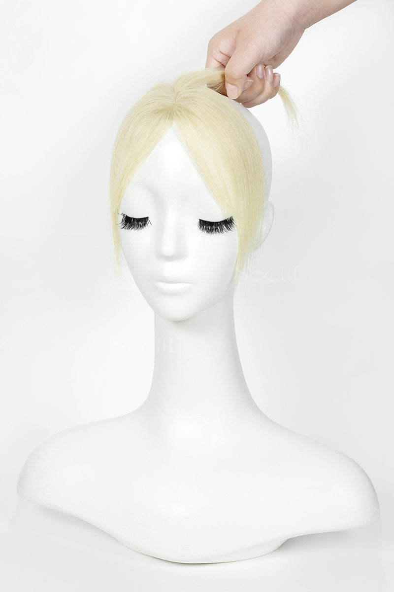 A blonde wig displayed on a white mannequin bust, with a hand holding the top section of the hair against a plain white background.