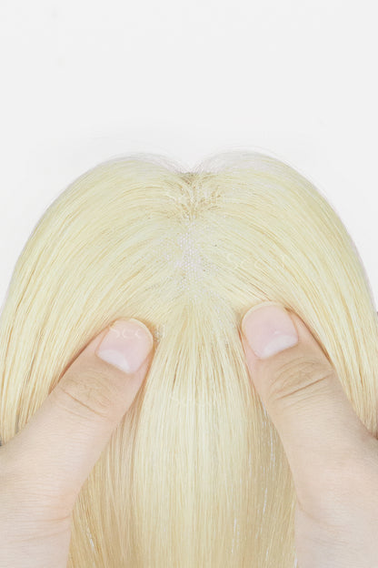 Close-up of a blonde wig or hairpiece from the top, showing fine hair strands and two fingers holding the sides apart against a plain white background.