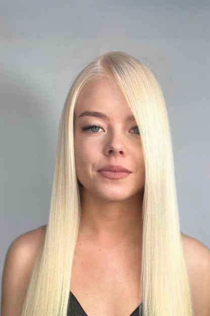 A close-up portrait of a woman with long, straight platinum blonde hair, wearing a black top against a plain gray background.