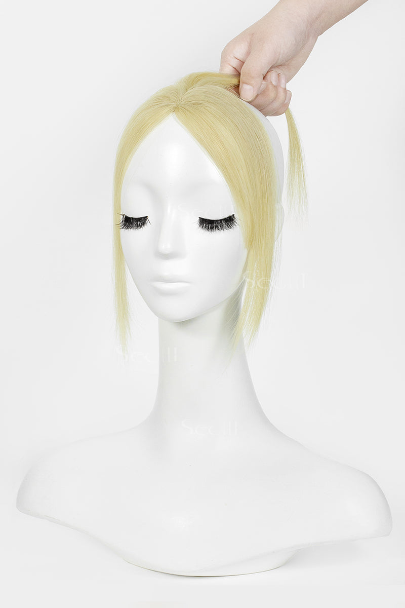 A blonde topper with a side-swept fringe and half-up style, displayed on a white mannequin head with a hand lifting the hair at the top against a plain white background.