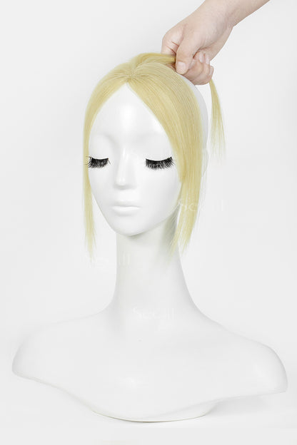 A blonde topper with a side-swept fringe and half-up style, displayed on a white mannequin head with a hand lifting the hair at the top against a plain white background.