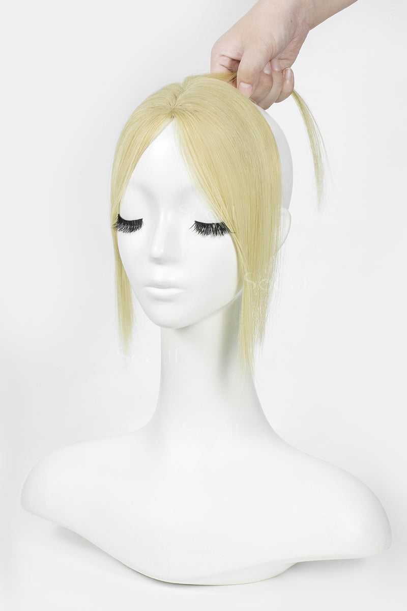 A blonde wig with side-swept bangs displayed on a white mannequin bust, with a hand lifting the hair at the top against a plain white background.