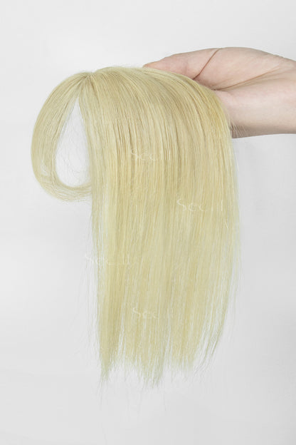 A hand holding a long, straight blonde hair extension or wig piece against a plain white background.