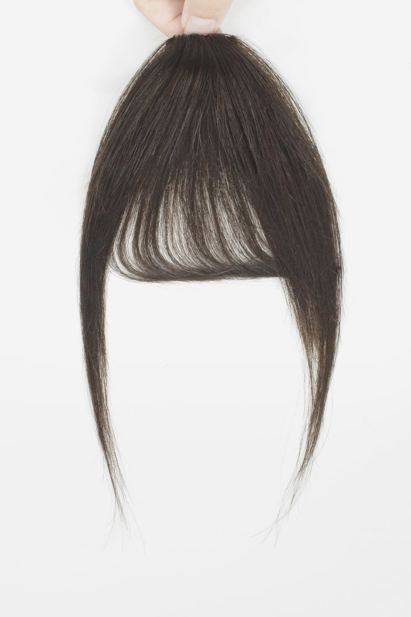 A dark brown hair extension piece with straight, layered bangs and long side-swept strands, held up by a hand against a plain white background.