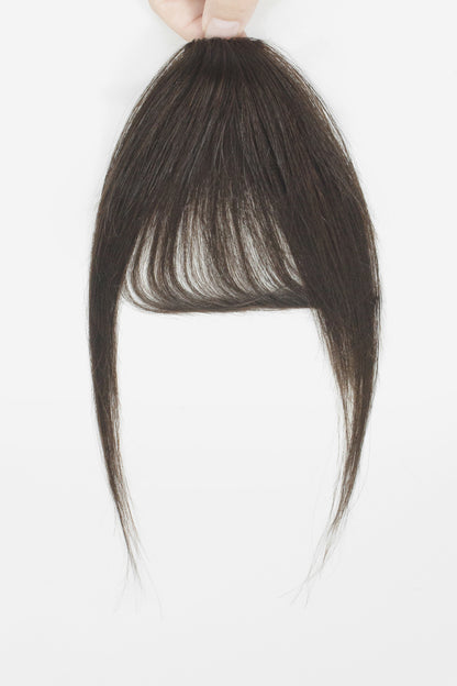 A dark brown hair extension piece with straight, layered bangs and long side-swept strands, held up by a hand against a plain white background.
