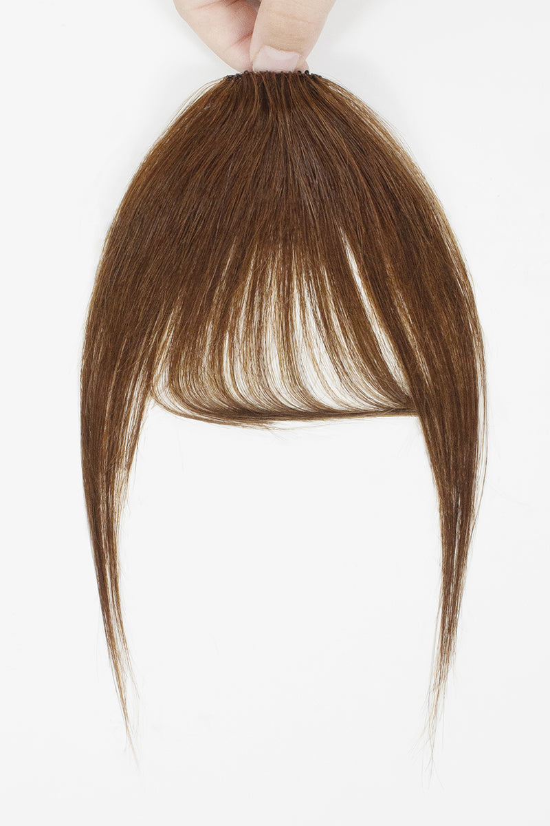 A brown hair extension piece with straight bangs and long side-swept strands, held up by a hand against a plain white background.