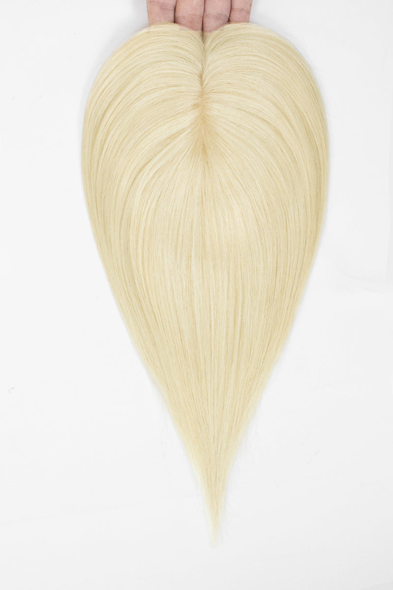 A heart-shaped blonde hair extension or wig piece held at the top by fingers against a plain white background.