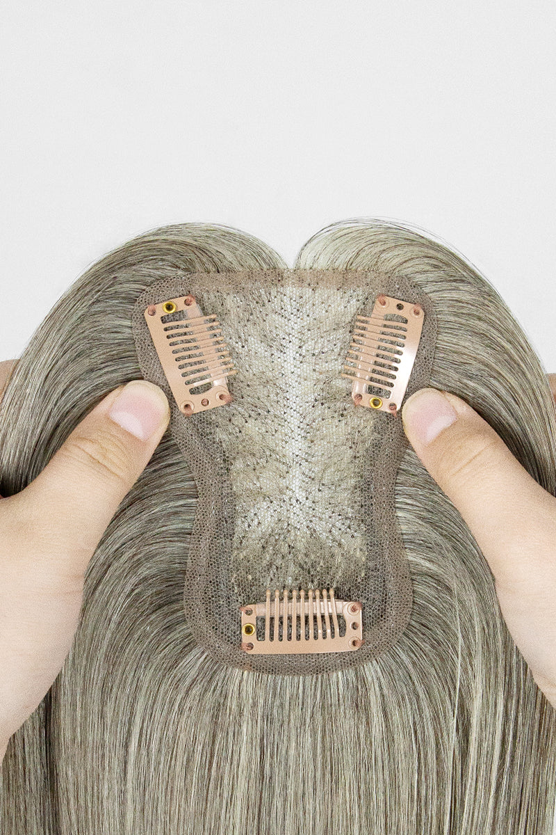 Close-up of a hairpiece with metal clips held by fingers against a white background