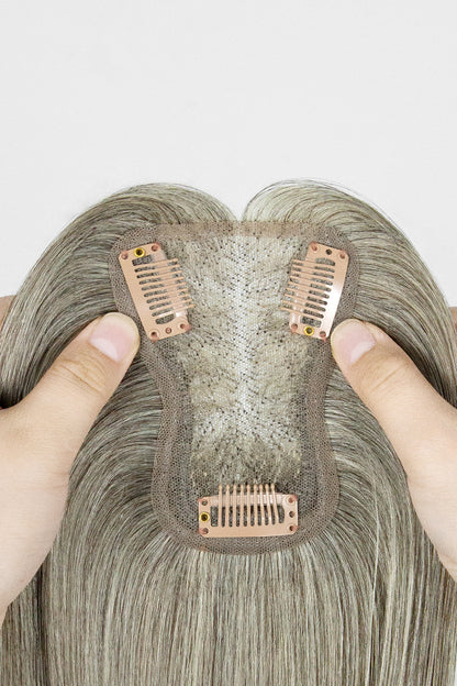 Close-up of a hairpiece with metal clips held by fingers against a white background