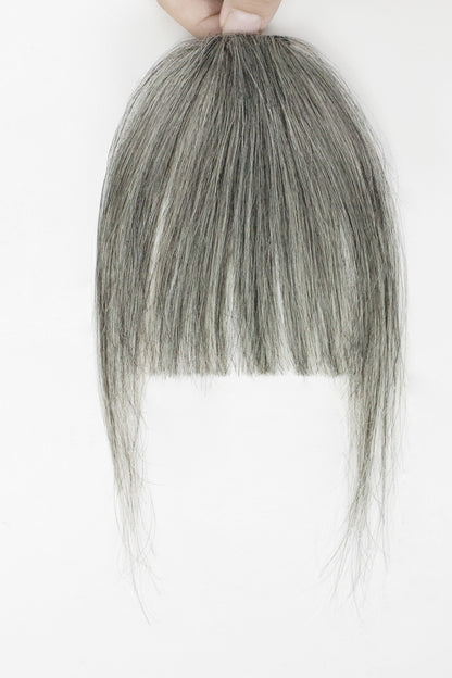 A gray synthetic wig with straight bangs held up by a hand against a plain white background.