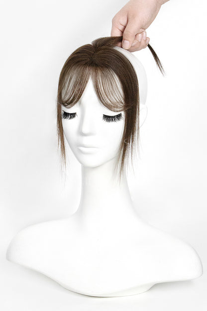 Mannequin head with a brown hairpiece being adjusted on a white background