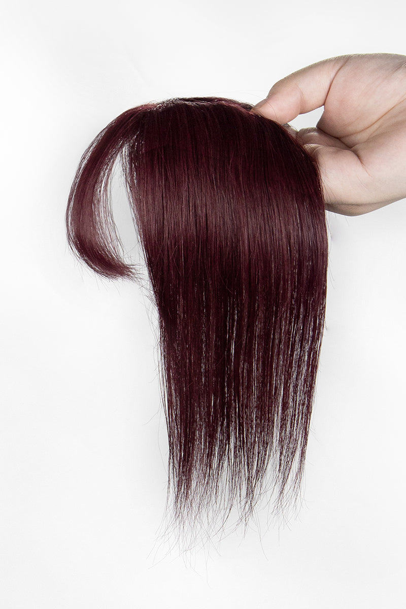 Burgundy hair topper held by a hand on a white background