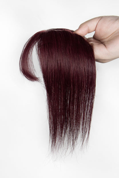 Burgundy hair topper held by a hand on a white background