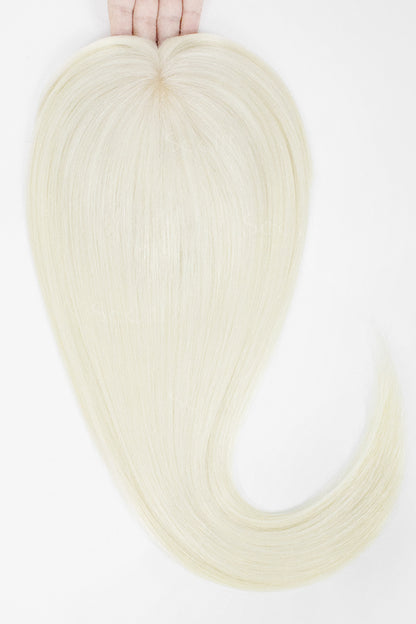 A hand holds up a long, straight synthetic hair extension piece in a very light platinum blonde color against a plain white background.