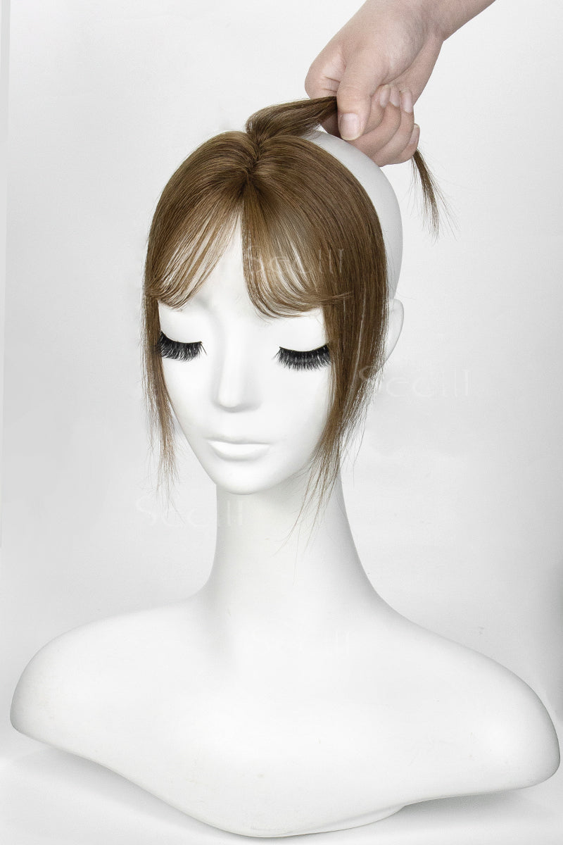 Mannequin head with a brown hair topper being adjusted on a white background