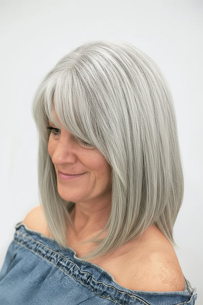 A woman with shoulder-length silver-gray hair wearing a straight, layered wig and a denim off-the-shoulder top, shown against a plain light background.