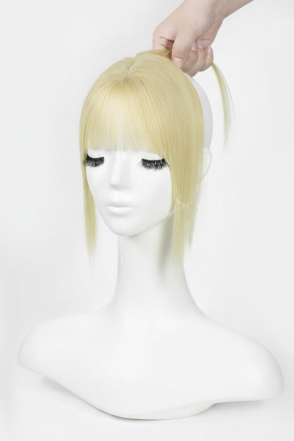 A blonde wig with straight bangs and a side ponytail, displayed on a white mannequin head with a hand adjusting the hair at the top against a plain white background.